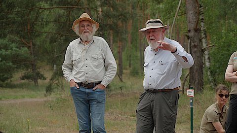 Zwei Männer im Gespräch miteinander. Im Hintergrund sind Bäume zu erkennen. Die Männer sind Prof. Michael Succow und Hannes Knapp
